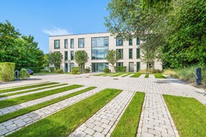 Ein modernes Gebäude mit einem gepflasterten Innenhof, grünen Rasenflächen und blauem Himmel.
