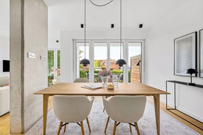 A modern dining area with a wooden table, two chairs, a vase with flowers, and a view through large windows. - Arrival amid the sea, light, and open landscape (List auf Sylt)