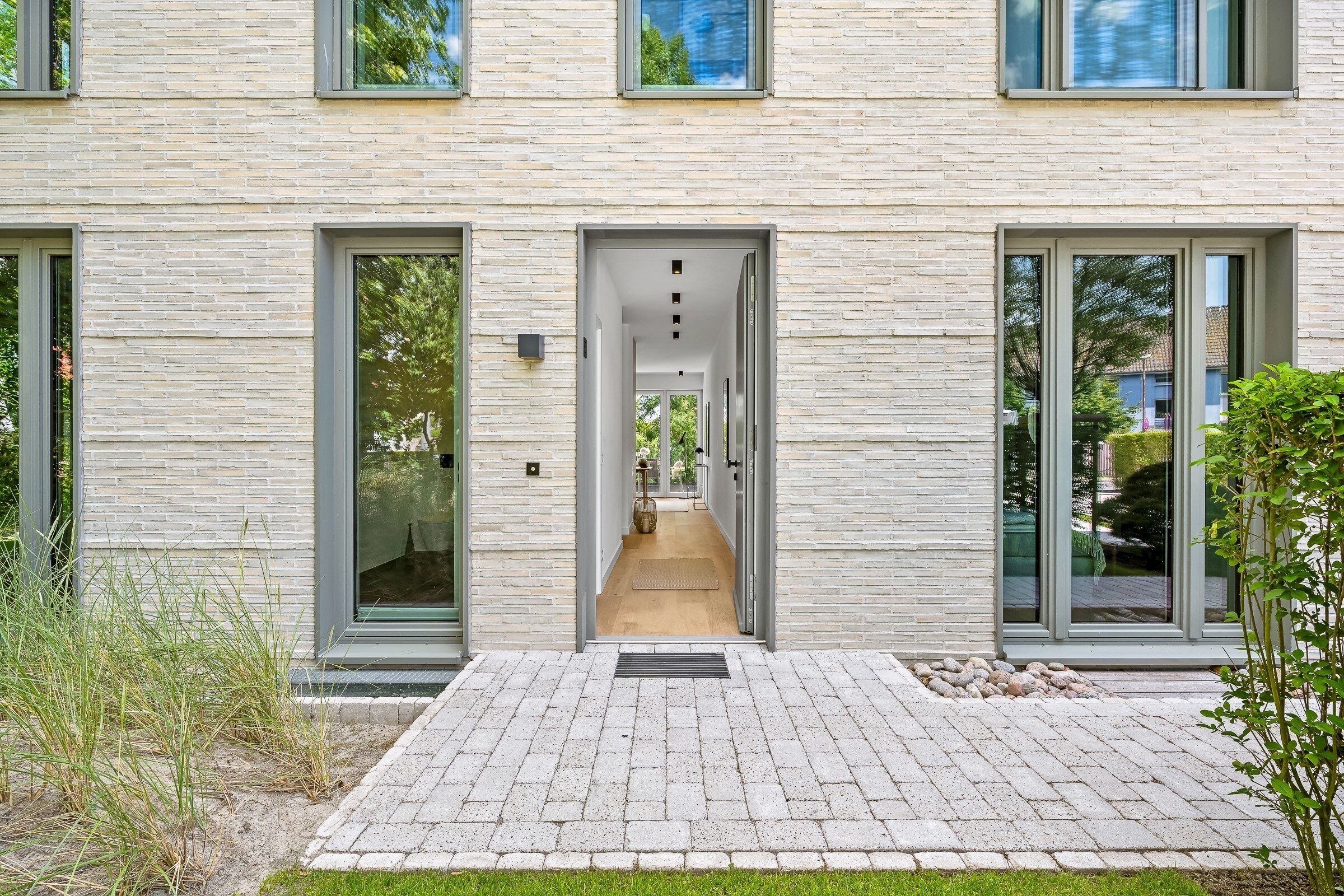 A modern building with a brick facade, large glass doors, and a paved entrance area.