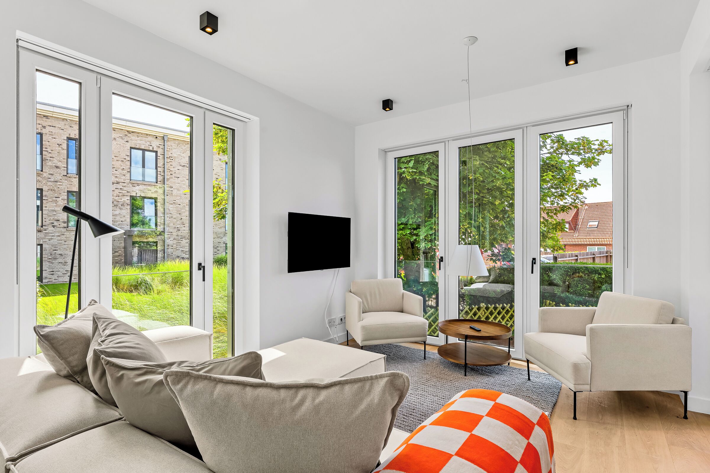 A modern living room with a sofa, armchairs, a coffee table, and a flat-screen TV mounted on the wall.