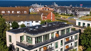 A multi-story building with large windows and balconies, surrounded by greenery and overlooking a body of water. - Arriving between the sea, the light, and the open landscape (List auf Sylt)