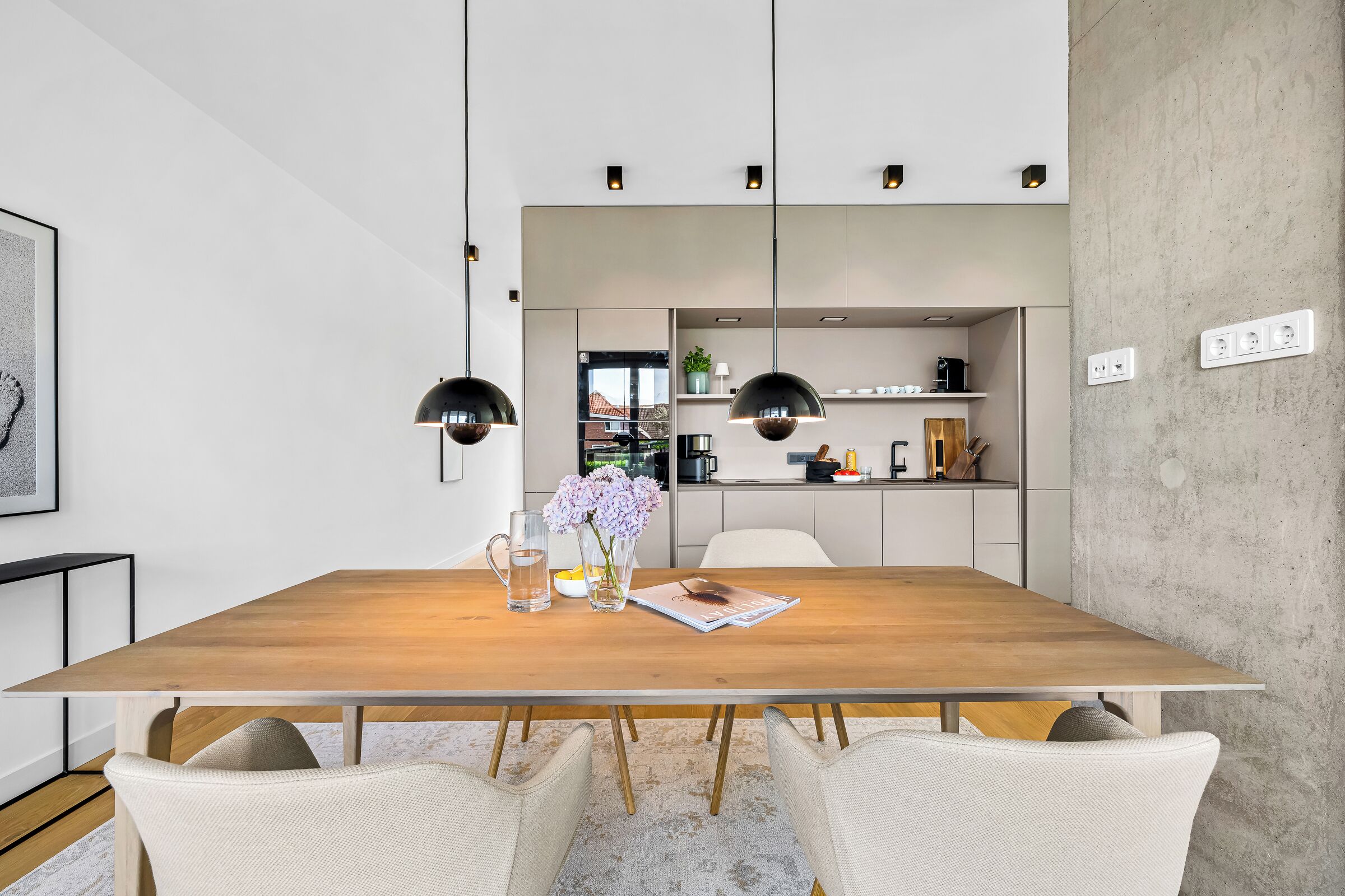 Een moderne eetruimte met een houten tafel, twee hanglampen en uitzicht op een keuken.