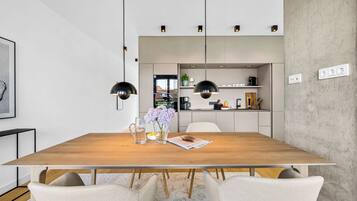 Een moderne eetruimte met een houten tafel, twee hanglampen en uitzicht op een keuken.