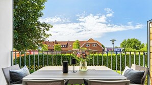 A balcony with a table and chairs, a vase with flowers, and a view of houses and a sign in the background. - Arriving between the sea, the light, and the open landscape (List auf Sylt)