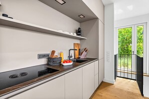 A modern kitchen with a black countertop, white cabinets, and a window with a view of greenery. - Arriving between the sea, the light, and the open landscape (List auf Sylt)
