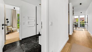 A modern interior with a hallway leading to a bedroom and a bathroom, featuring a wooden floor, white walls, and a door with a towel rack. - Arriving between the sea, the light, and the open landscape (List auf Sylt)