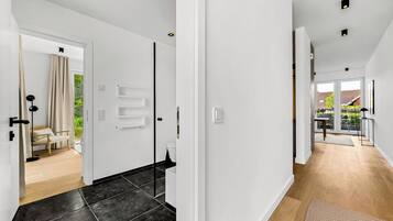 Een modern interieur met een gang die leidt naar een slaapkamer en een badkamer, met een houten vloer, witte muren en een deur met een handdoekhouder.