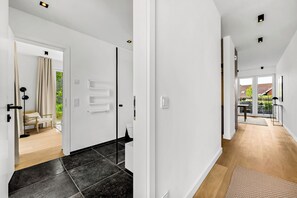 A modern interior with a hallway leading to a bedroom and a bathroom, featuring a wooden floor, white walls, and a door with a towel rack. - Arriving between the sea, the light, and the open landscape (List auf Sylt)