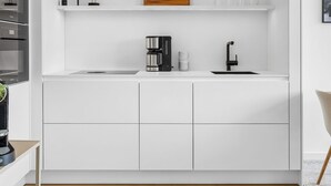A modern kitchen with white cabinetry, a black faucet, and a wooden accent wall. - Arriving between the sea, the light, and the open landscape (List auf Sylt)
