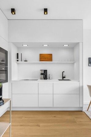 A modern kitchen with white cabinetry, a black faucet, and a wooden accent wall. - Arriving between the sea, the light, and the open landscape (List auf Sylt)