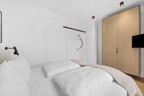 A modern bedroom with a bed, a bedside lamp, a wooden wardrobe, and a mounted TV. - Arriving between the sea, the light, and the open landscape (List auf Sylt)
