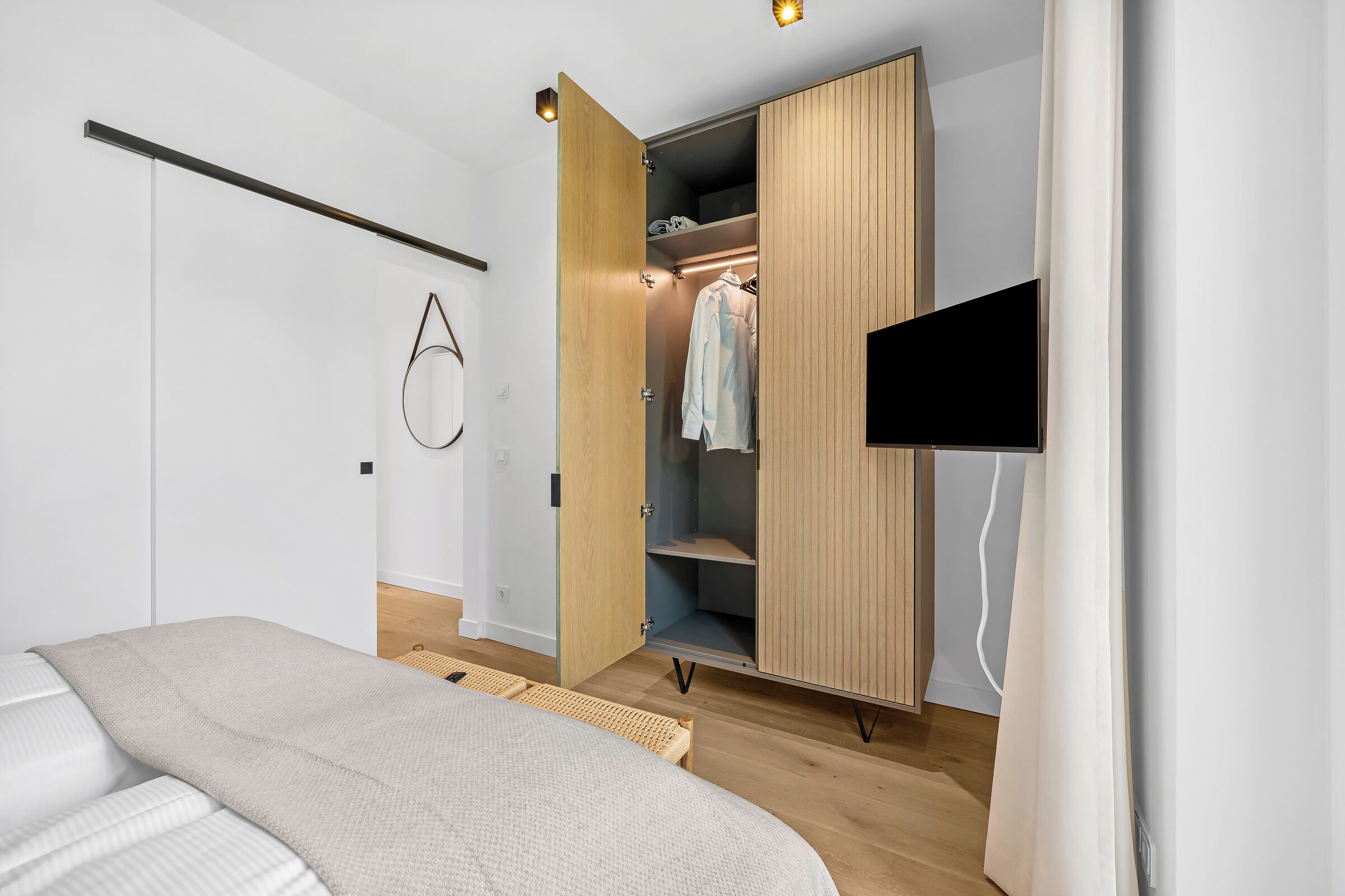 Una camera da letto con un letto, un armadio, una TV e un portalampada circolare fissato al muro.