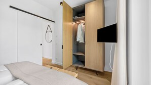 A bedroom with a bed, a wardrobe, a TV, and a wall-mounted circular light fixture. - Arriving between the sea, the light, and the open landscape (List auf Sylt)