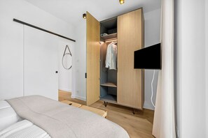 A bedroom with a bed, a wardrobe, a TV, and a wall-mounted circular light fixture. - Arriving between the sea, the light, and the open landscape (List auf Sylt)