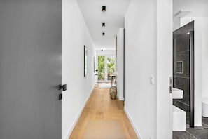 Un couloir moderne avec un plancher en bois, des murs blancs et une porte donnant sur une salle de bain carrelée de carreaux foncés.