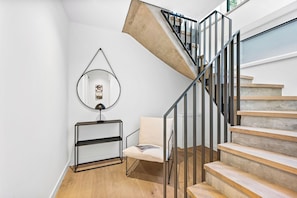 Un escalier moderne avec une rampe en verre, un plancher en bois, une structure en métal noir et un mur blanc.