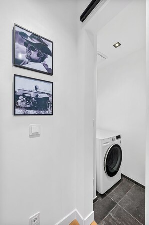 Ein Waschraum mit einer Waschmaschine, zwei gerahmten Bildern an der Wand und einem Lichtschalter.