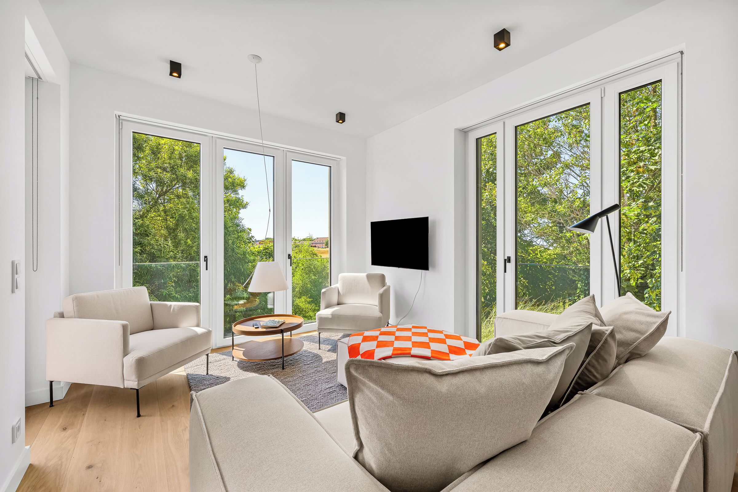 A spacious living room with a large sofa, a coffee table, and a TV mounted on the wall.