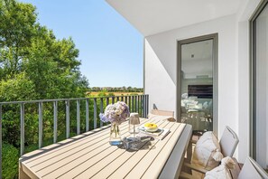 Un balcon avec une table dressée pour deux personnes, un vase de fleurs et une vue sur la verdure et les bâtiments.