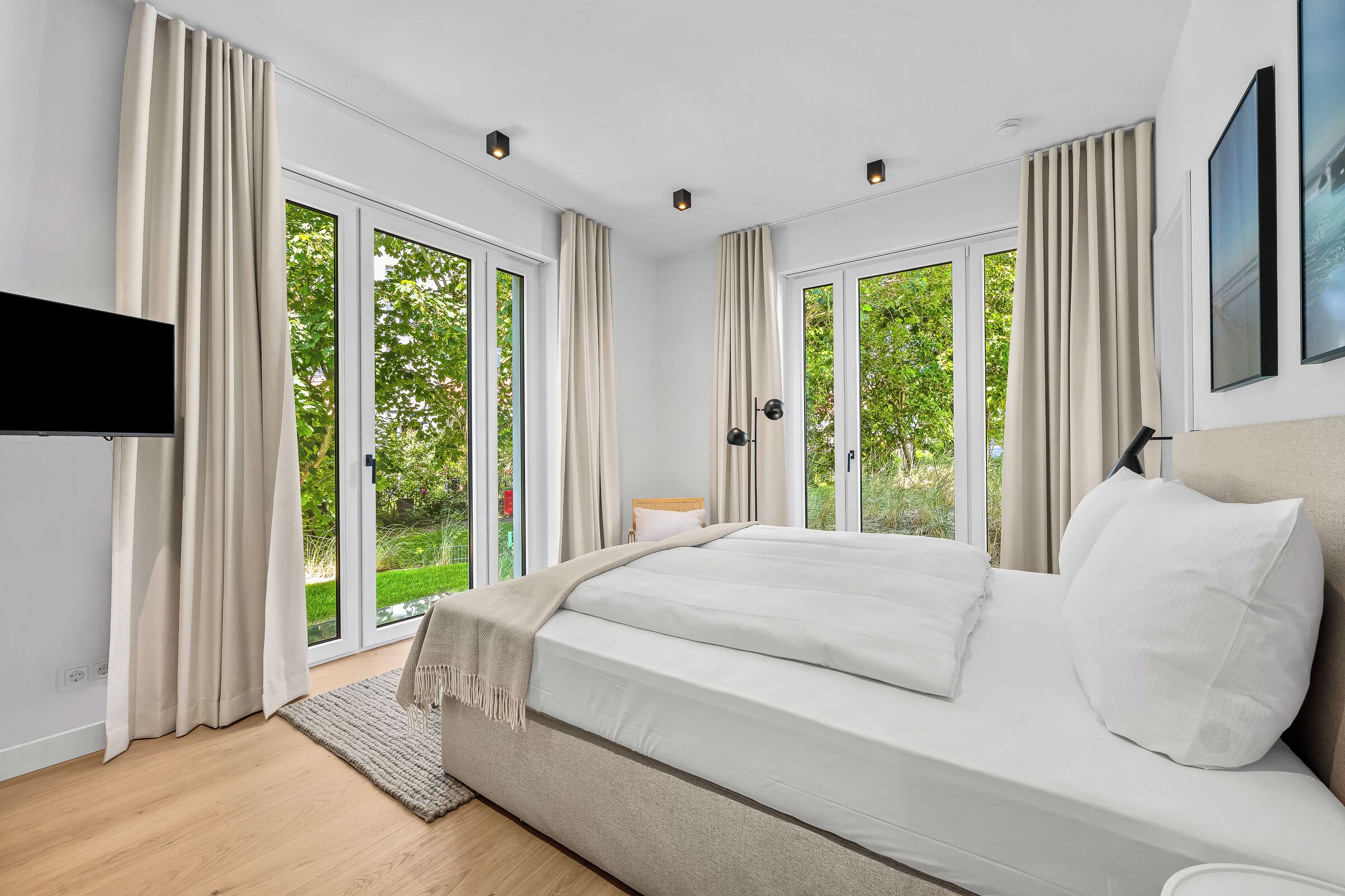 Une chambre moderne avec un grand lit, des portes-fenêtres coulissantes donnant sur un jardin et un téléviseur à écran plat fixé au mur.