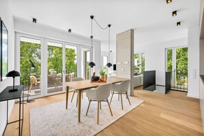 A modern dining area with a wooden table, four chairs, a rug, and pendant lighting.