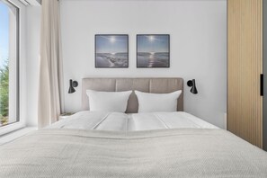 Een slaapkamer met een bed, twee wandlampen en twee foto’s in lijsten.