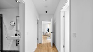 A hallway with a white sink, a round mirror, and a door leading to a room with a light-colored floor. - Arriving between the sea, the light, and the open landscape (List auf Sylt)