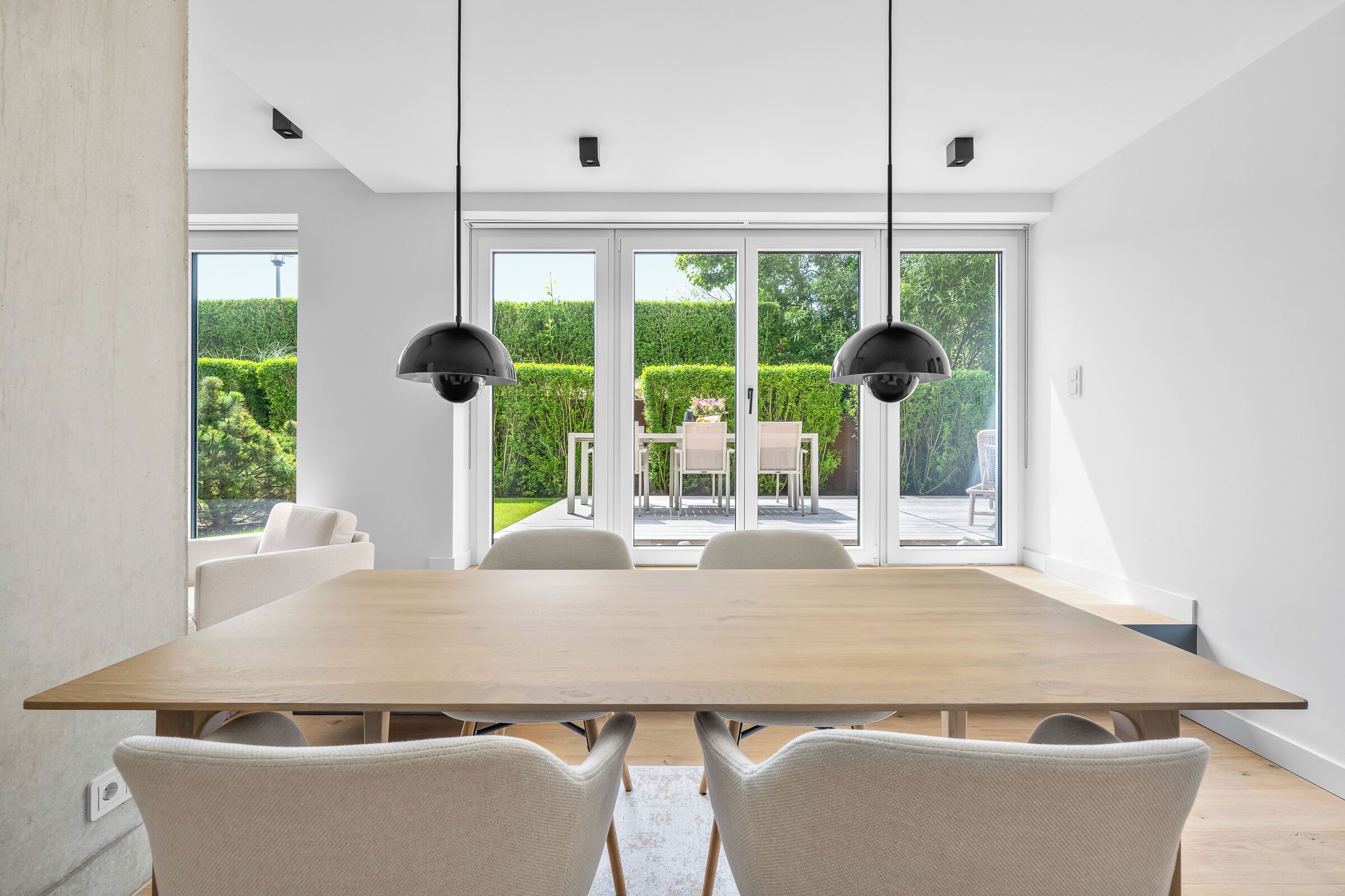 Un espace de salle à manger moderne avec une grande table en bois, des chaises blanches et des luminaires suspendus.