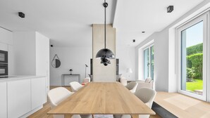 A modern kitchen with white cabinetry, a wooden dining table, and a large window offering a view of greenery. - Arriving between the sea, the light, and the open landscape (List auf Sylt)
