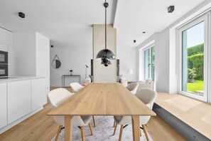 Eine moderne Küche mit weißen Schränken, einem Holztisch und einem großen Fenster mit Blick auf Grünflächen.