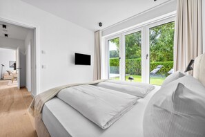 Ein Schlafzimmer mit einem großen Bett, einem an der Wand befestigten Fernseher und einer Glastür, die in einen Garten führt.
