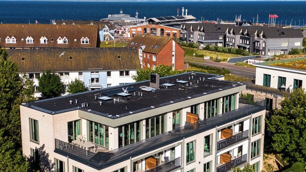 A multi-story building with large windows and balconies, surrounded by greenery and overlooking a body of water. - Arriving between the sea, the light, and the open landscape (List auf Sylt)