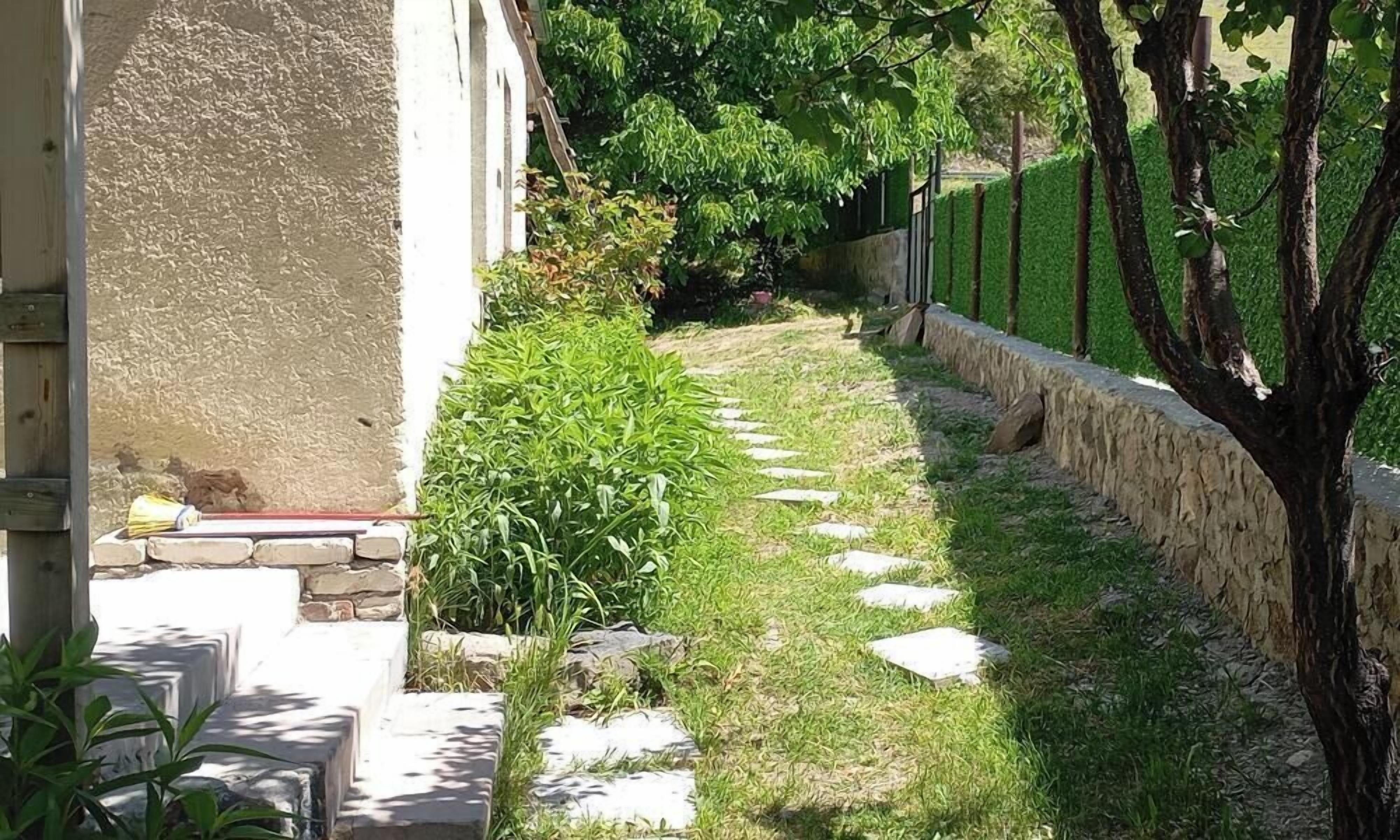 A garden pathway with a stone wall, steps, and greenery.