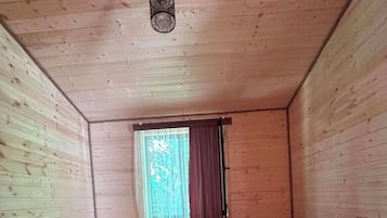 A wooden cabin room with two beds, a small table, a window with curtains, and a hanging light fixture.