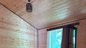 A wooden cabin room with a bed, a small table, and a window with curtains.