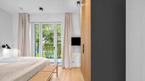 A modern bedroom with a bed, bench, TV, and a view of greenery through a glass door. - Arriving between the sea, the light, and the open landscape (List auf Sylt)