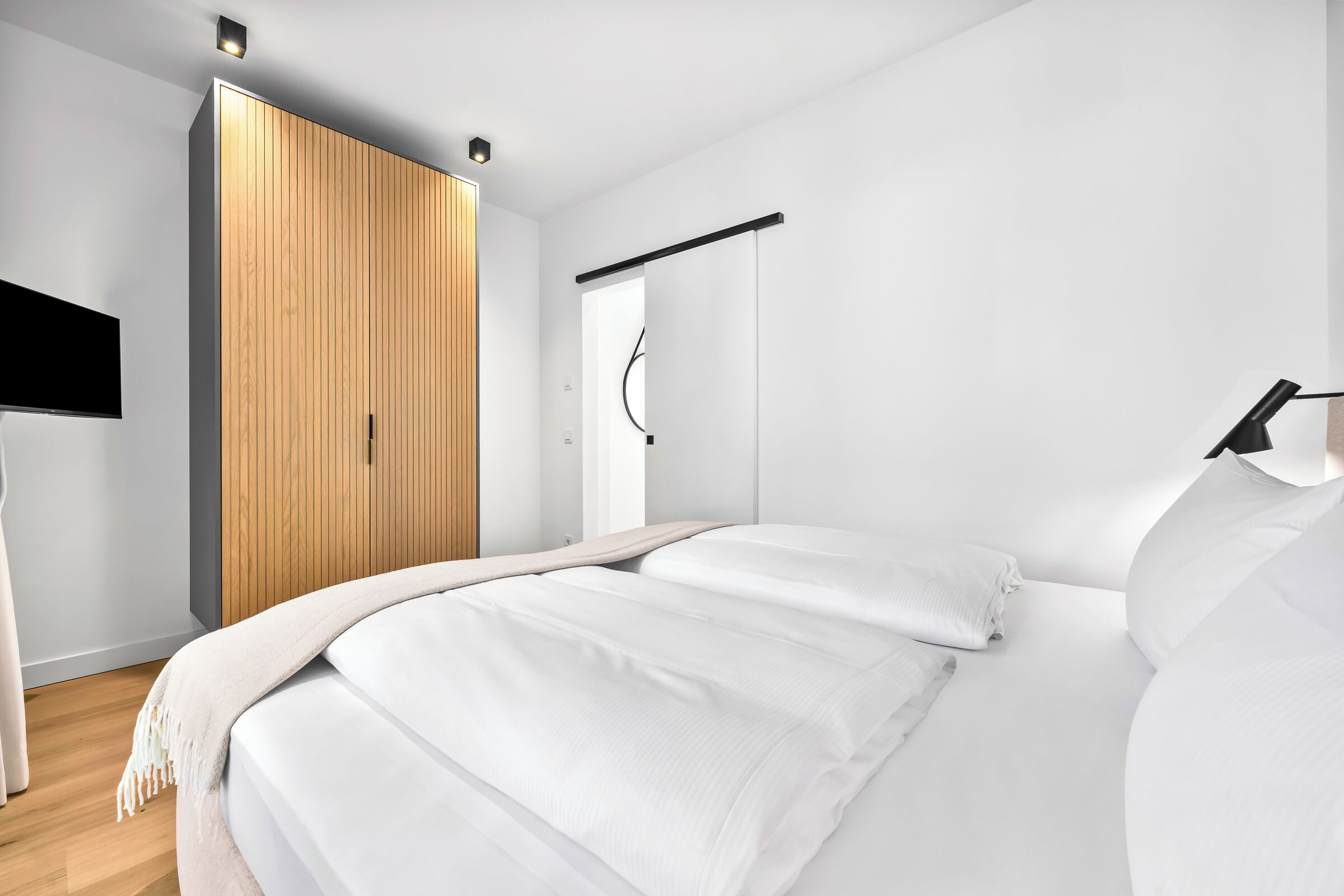 A modern bedroom with a bed, wooden wardrobe, and a black hanging rod.