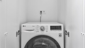 A compact, white LG ThinQ washing machine in a small, enclosed laundry room with a wooden floor. - Arriving between the sea, the light, and the open landscape (List auf Sylt)