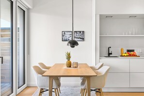 Ein moderner Essbereich mit Holztisch, vier Stühlen, einer Pendelleuchte und einer Küche mit Obstschale.
