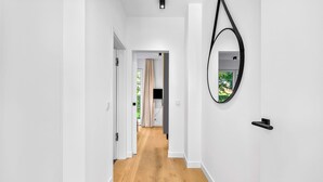 A hallway with white walls, a wooden floor, and a door leading to another room. - Arriving between the sea, the light, and the open landscape (List auf Sylt)