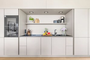 Une cuisine moderne avec des meubles blancs, un four à micro-ondes encastré, un évier et un plan de travail agrémenté d’ustensiles de cuisine et d’une plante.
