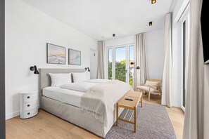 Une chambre à coucher moderne avec un grand lit, une table de chevet, une chaise et une fenêtre avec des rideaux.