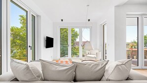 Un soggiorno moderno con un divano, una TV a schermo piatto e vista su una zona esterna attraverso ampie vetrate.