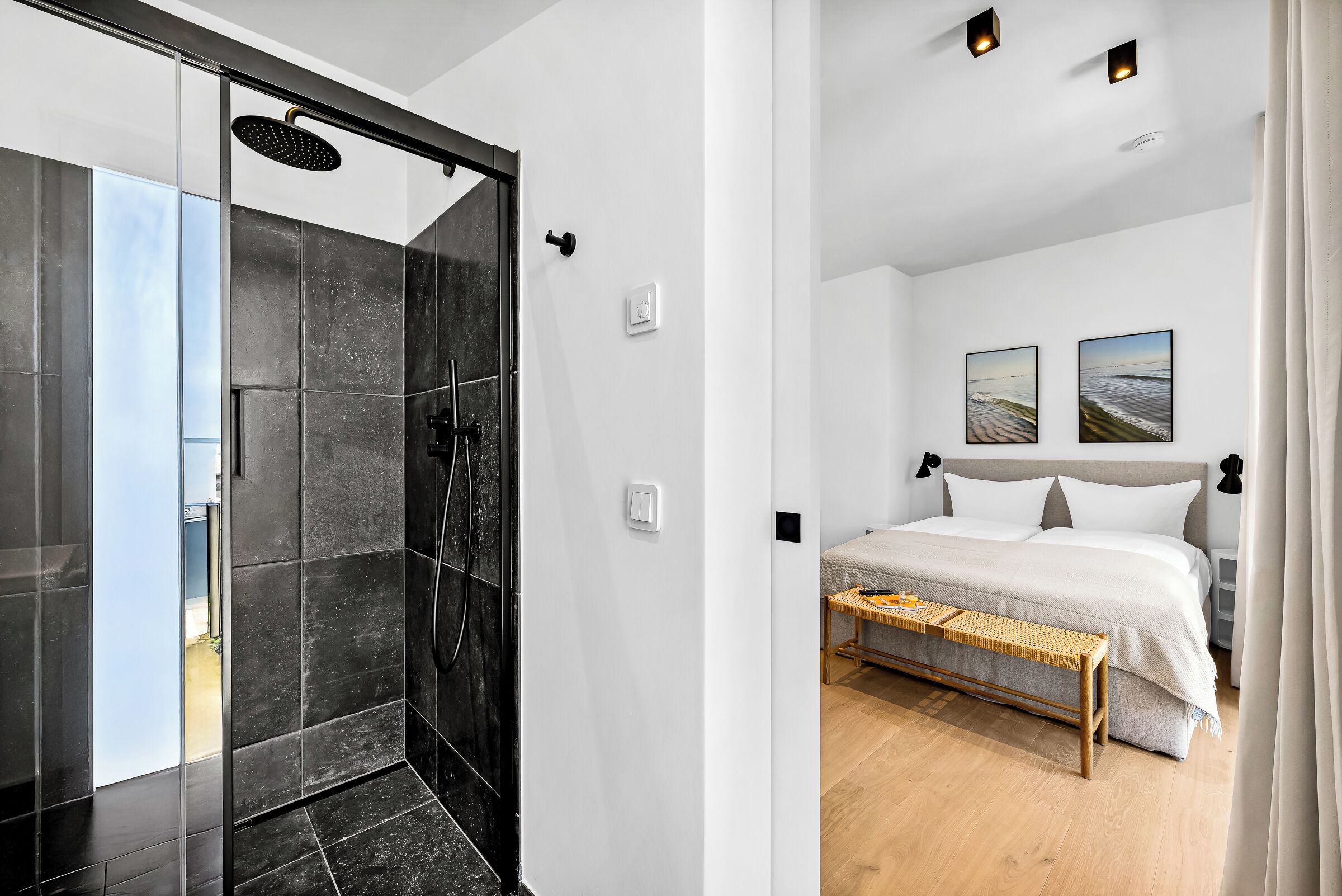 Un bagno moderno con box doccia in vetro, un letto con biancheria da letto bianca e due quadri appesi al muro.
