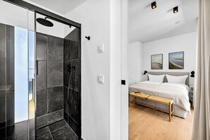 Ein modernes Badezimmer mit Duschabtür aus Glas, einem Bett mit weißer Bettwäsche und zwei gerahmten Bildern an der Wand.