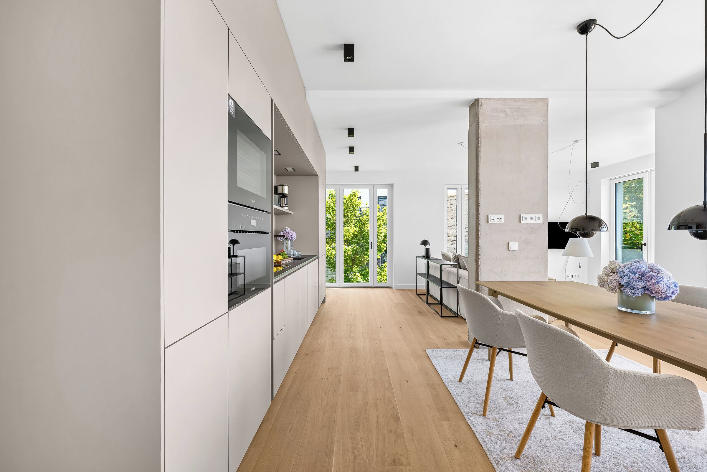 Eine moderne Küche mit weißen Schränken, einem Holztisch und Blick auf Grünfläche.