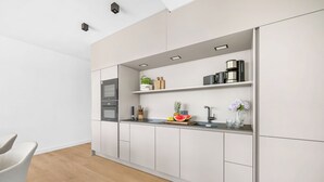 Una cucina moderna con mobili bianchi, forno integrato e un piano di lavoro con diversi elettrodomestici e frutta e verdura fresca.