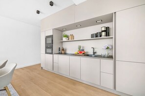 Eine moderne Küche mit weißen Schränken, einem Einbauofen und einer Arbeitsplatte mit verschiedenen Geräten und frischem Obst und Gemüse.