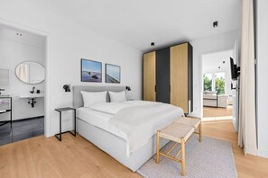 Ein modernes Schlafzimmer mit Bett, Nachttischen, einem Spiegel und Blick auf den Wohnbereich.