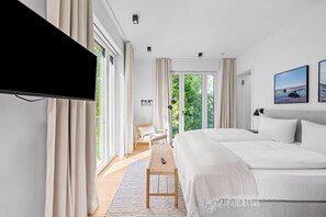 A modern bedroom with a large bed, a flat-screen TV, a desk, and a chair. - Arriving between the sea, the light, and the open landscape (List auf Sylt)
